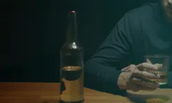 Человек с бутылкой алкоголя и стаканом